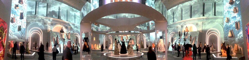 Dior exhibit main room with many dresses and dreamy cloud projections on walls throughout the room 
